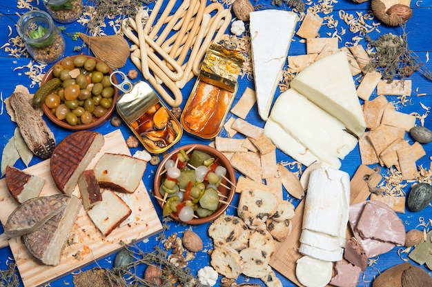 Foto mesa posta com um aperitivo composto por diferentes alimentos queijos e latas de pickles