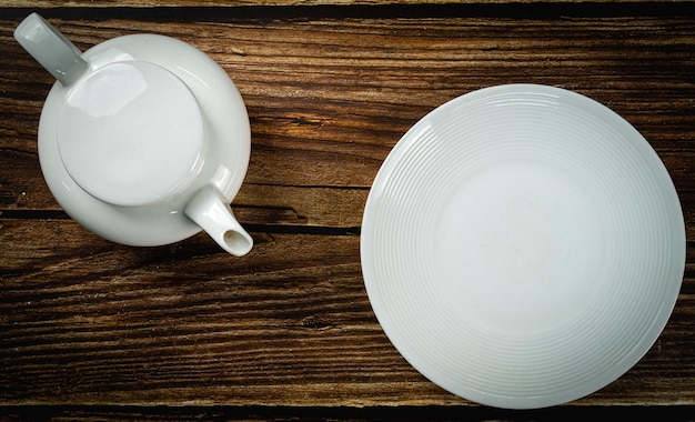 Mesa preparada con plato blanco y tetera en la vista superior de fondo de madera