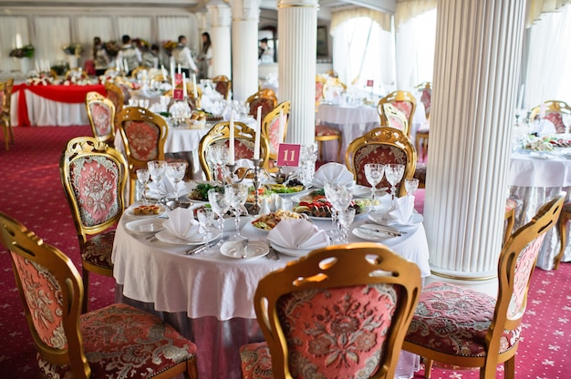 Mesa puesta en el banquete de bodas en el restaurante, estilo clásico con manteles y servilletas blancas, jarrones con flores.