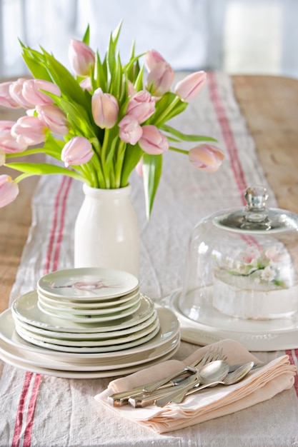 Una mesa puesta para una comida con un jarrón de tulipanes rosas