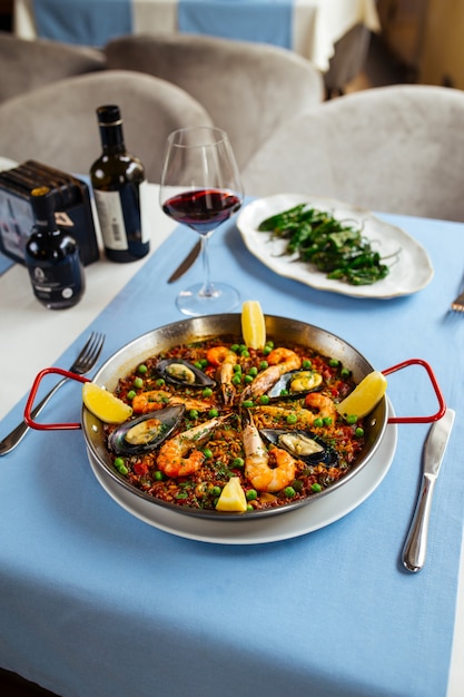 Mesa de restaurante servida con platos españoles paella de marisco y pimientos de padrón