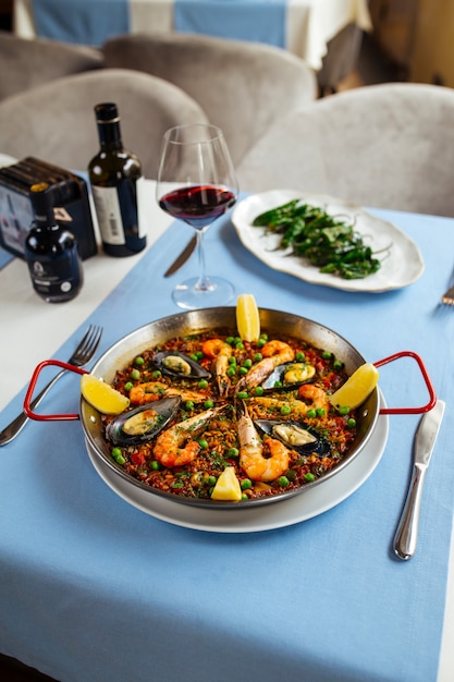 Mesa de restaurante servida con platos españoles paella de marisco y pimientos de padrón