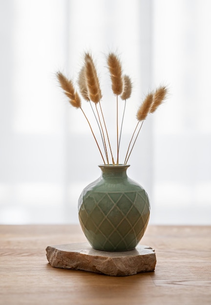 Foto mesa de roble de madera con un jarrón verde con flores secas y piedra