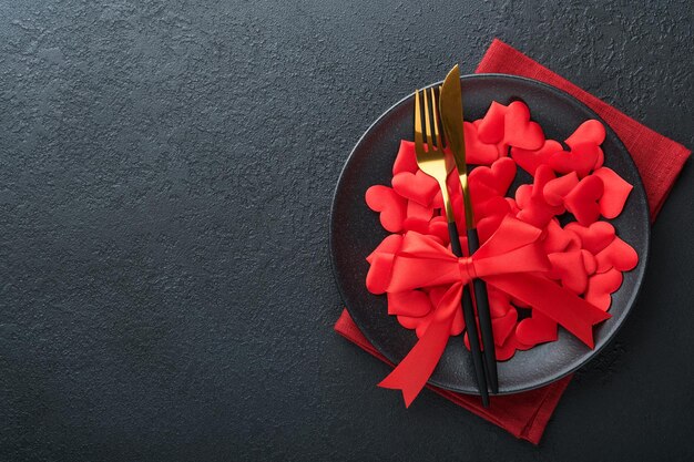 Mesa romántica del día de San Valentín Vacío o primer plano de una cena plato negro cuchillo tenedor y corazones de seda decorativos sobre fondo negro Concepto de vacaciones Copiar espacio para inscripciones