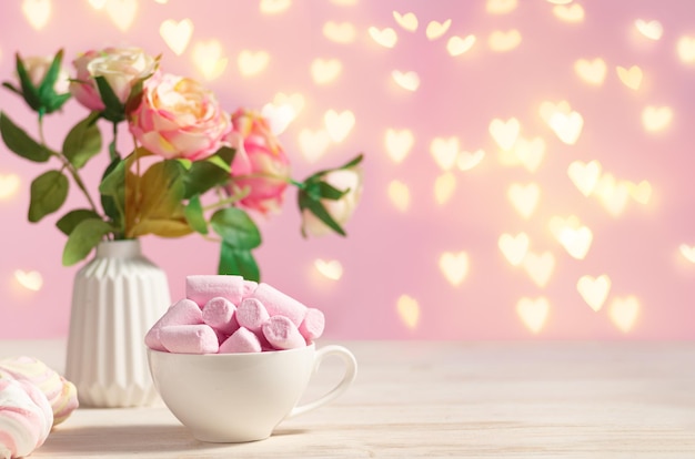 Mesa romántica festiva decorada con flores y una taza con malvaviscos poink