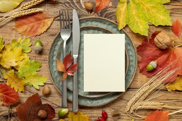 Mesa rústica de otoño con tarjeta en blanco entre hojas y maqueta de vista superior de bayas