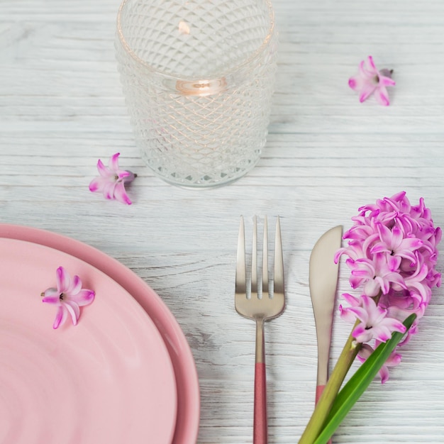 Mesa rústica rosa con velas de flores de jacinto púrpura y servilleta de lino sobre una mesa de madera blanca