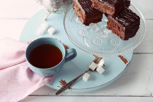 Mesa servida con una tetera, una taza de té y pasteles de chocolate en primer plano de fondo azul y blanco