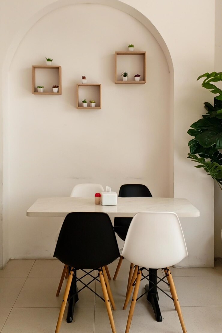 una mesa con sillas blancas y negras y una planta en la pared en el restaurante de la cafetería