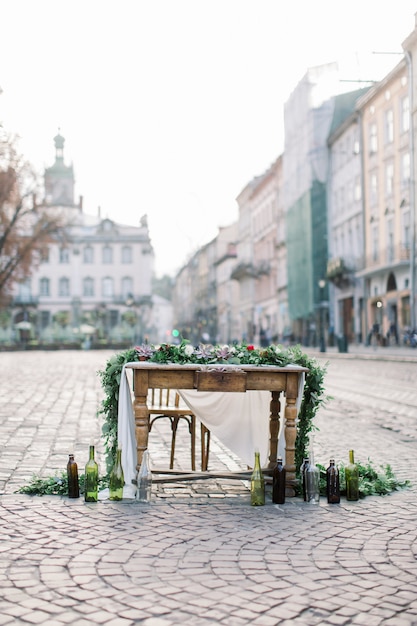 Mesa y sillas de madera decoradas con flores, suculentas y decoración. Botellas de vidrio con velas. Mesa decorada en el pavimento de piedra en la ciudad vieja de Lviv