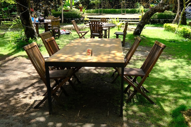 mesa y sillas de madera marrón en un sombreado jardín tropical. el patio está cubierto de hierba verde.