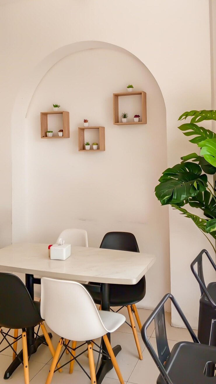 una mesa con sillas negras y blancas una planta en la esquina y una planta en el muro en la cafetería