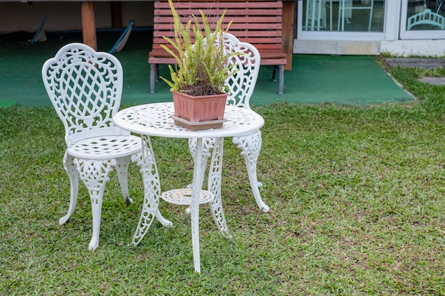 Mesa y sillas vintage blanco con planta de helecho en un jarrón en el patio de césped