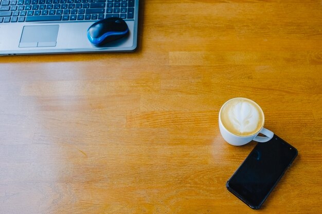 Mesa con taza de café con leche, computadora y teléfono inteligente.