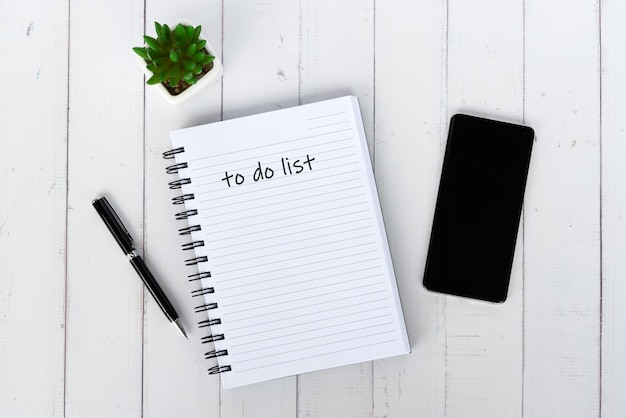 Mesa con teléfono inteligente y bloc de notas con texto para hacer la lista
