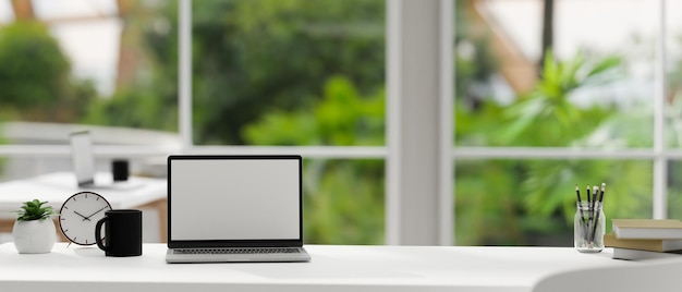 Mesa de trabajo blanca moderna con maqueta de computadora portátil sobre una oficina verde borrosa en el fondo