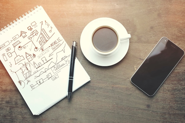 Mesa de trabajo: cuaderno, bolígrafo, teléfono y taza de café en la mesa de madera