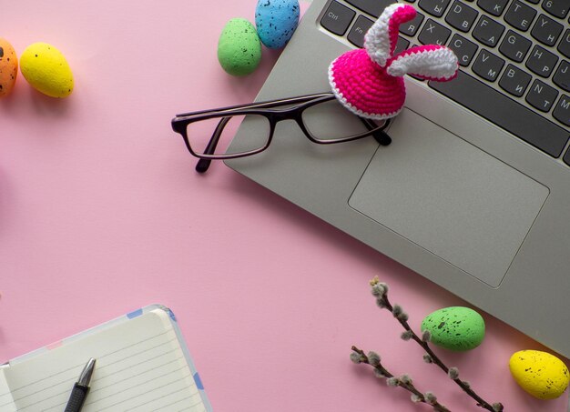 Mesa de trabajo con dispositivos y huevos multicolores de vacaciones de pascua sobre fondo rosa