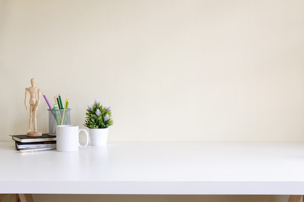 Mesa de trabajo con espacio de copia taza de café, plat, cuaderno y jarra de lápiz en la mesa blanca.