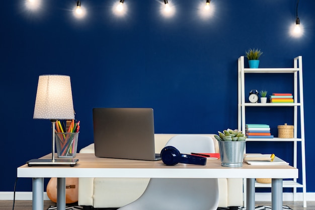 Foto mesa de trabajo con ordenador portátil contra la pared azul en piso moderno