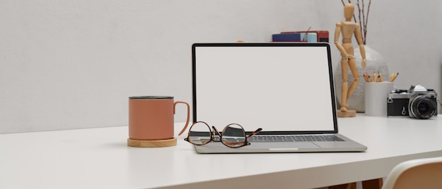 Mesa de trabajo simple con maqueta portátil, vasos, taza y suministros en mesa blanca con silla blanca