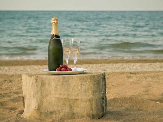 Mesa de un trozo de madera con una botella de champán y fresas junto al mar.