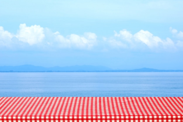 Mesa vacía con mantel rojo y blanco sobre mar borrosa al aire libre