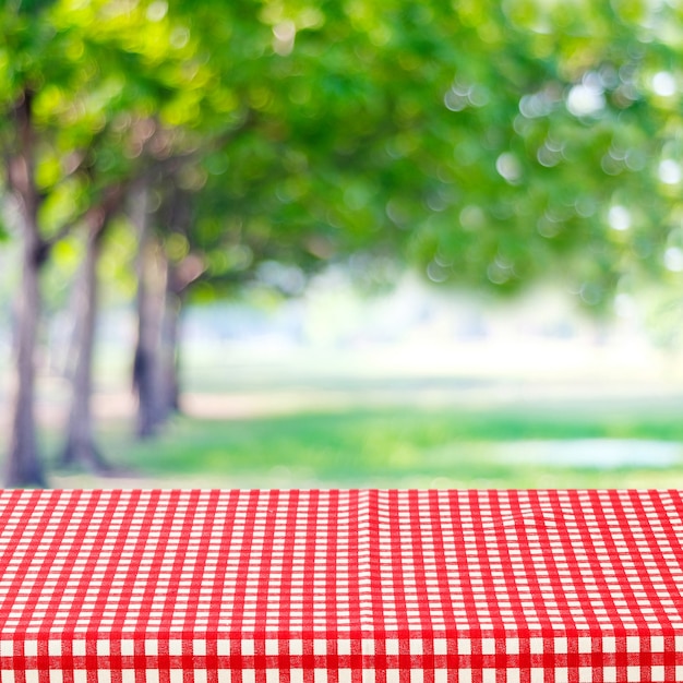 Foto mesa vacía con mantel rojo y blanco sobre parque borroso