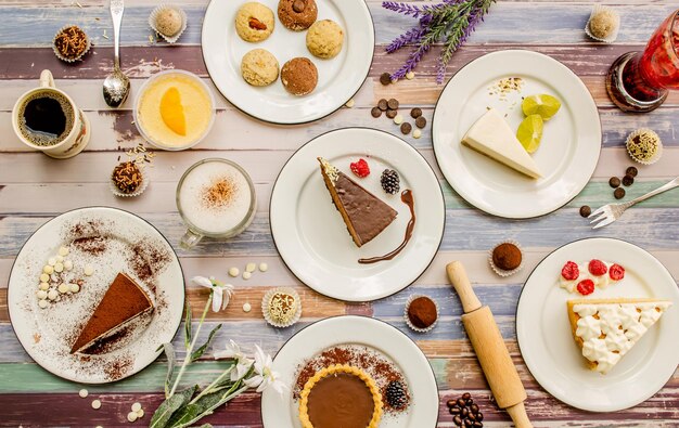 Foto mesa con varias galletas, donuts, pasteles, tartas de queso y postres sobre fondo blanco. delicioso