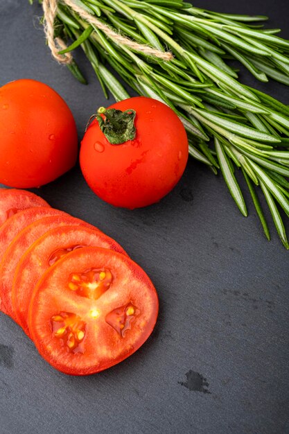 Foto mesa de verduras. pepinos, tomates y romero en una mesa negra