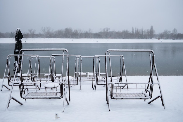 Mesas e cadeiras sob a neve em um café ao lado do lago durante o dia de inverno