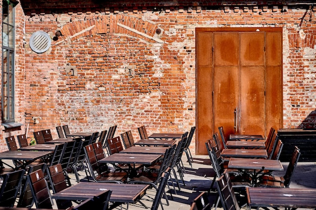 Mesas e cadeiras vazias de um café ao ar livre contra o pano de fundo de uma velha parede de tijolos com porta em um
