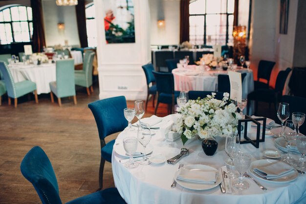 Mesas redondas no restaurante com toalhas de mesa brancas e buquês de flores brancas na decoração