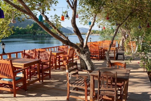 Mesas vacías de madera en un restaurante en la orilla del río Árbol con linternas de colores Horizontal