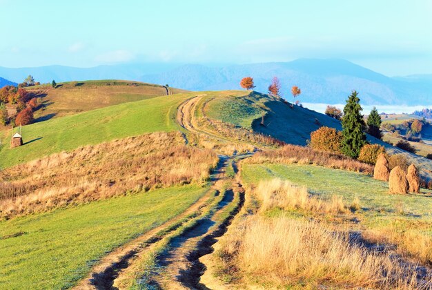 Meseta de la mañana brumosa del otoño con la pila de heno y el camino sucio del país (afueras de la aldea de Mighgirya, Mt's de los Cárpatos, Ucrania).