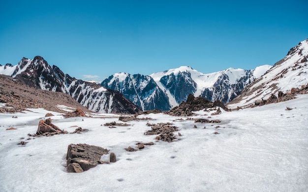 Meseta nevada de gran altitud. Paisaje alpino panorámico con picos nevados y rocas afiladas bajo un cielo azul. Colorido paisaje de montaña soleada con la cima de la montaña nevada.