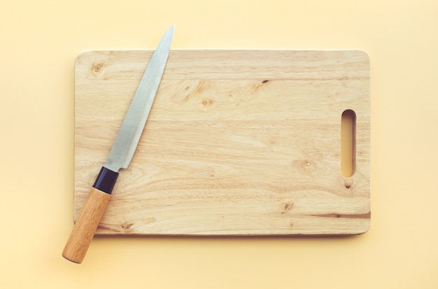 Messer auf hölzernem Schneidebrett auf pastellfarbenem Hintergrund