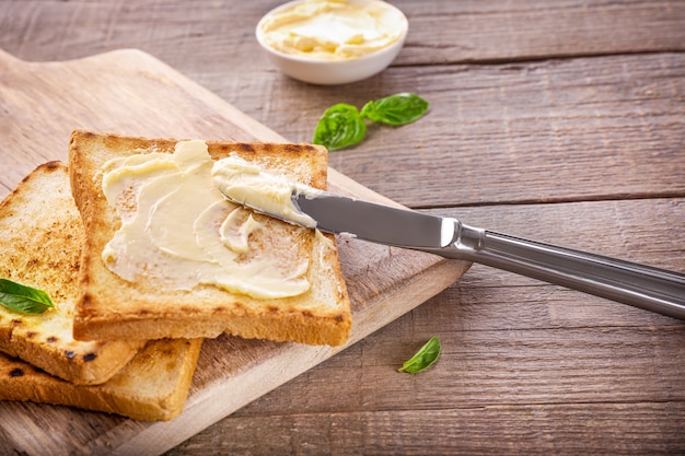 Messer, das Butter auf Toastbrot auf Holz verteilt