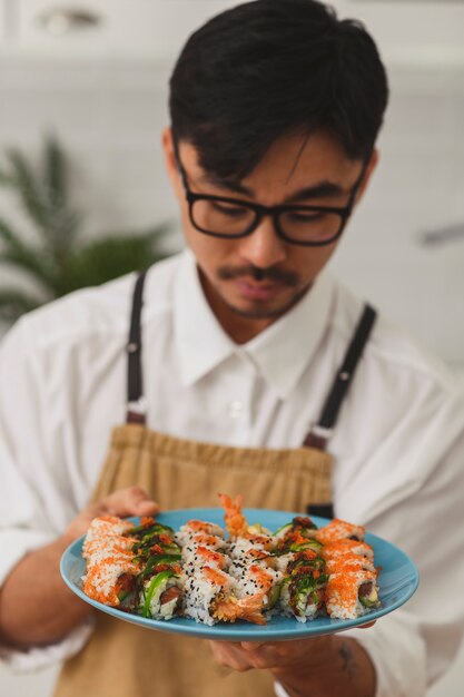 Mestre asiático preparando sushi em um homem do restaurante em pé na cozinha e polvilhando sementes de gergelim