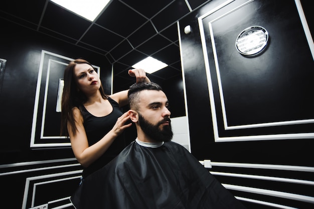 Mestre corta cabelo e barba de homens na barbearia, cabeleireiro faz penteado para um jovem.