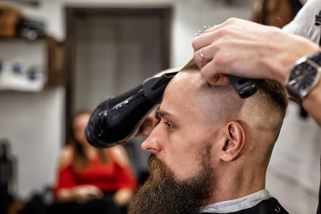 Mestre corta cabelo e barba de homens na barbearia, cabeleireiro faz penteado para um jovem