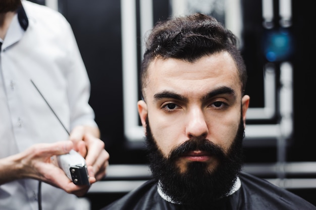 Mestre corta cabelo e barba de homens na barbearia, cabeleireiro