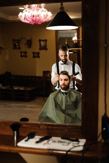 Mestre corta cabelo e barba de homens na barbearia