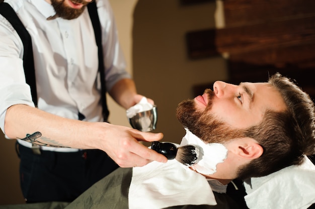 Mestre corta cabelo e barba de homens na barbearia