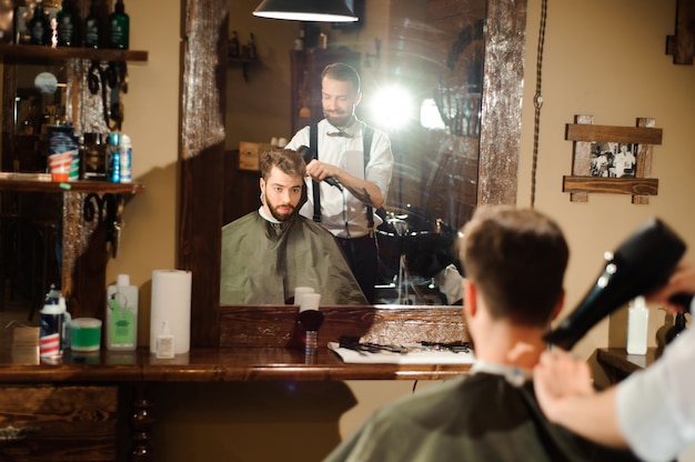 Mestre corta cabelo e barba de homens na barbearia