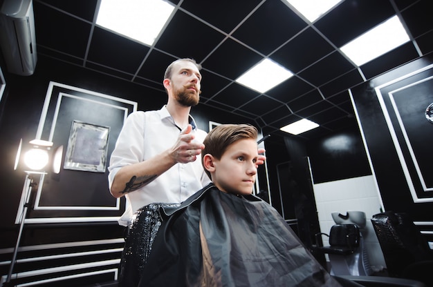 Mestre corta o cabelo de um menino na barbearia