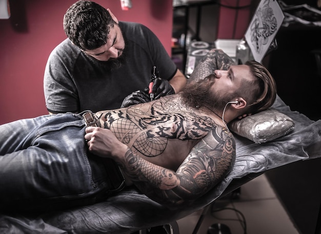 Mestre da arte da tatuagem faz tatuagem na pele de seu cliente em seu salão