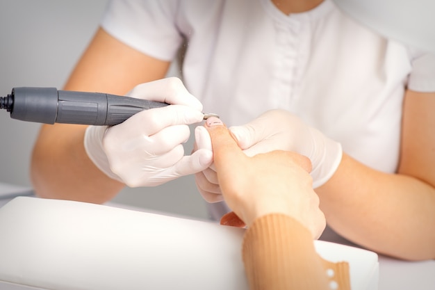 Mestre de manicure aplicando máquina elétrica de lixa de unha removendo esmalte velho das unhas em um salão de beleza