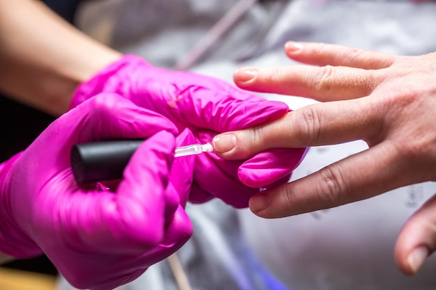 Mestre de manicure em luvas cor de rosa, raspando a velha camada de verniz no salão de manicure usando broca Manicure profissional na clínica de cosmetologia Higiene para os pés no salão de beleza