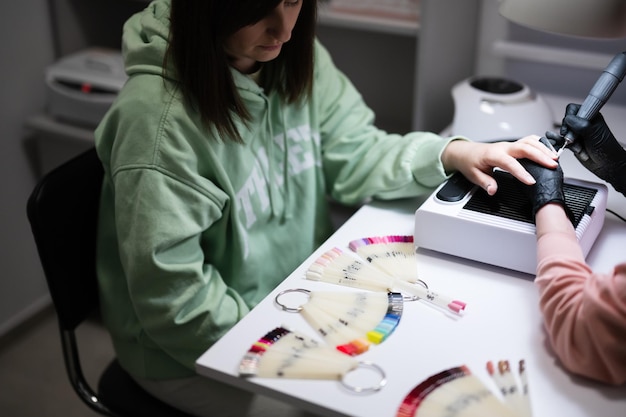 Mestre de manicure trabalhando com cliente do sexo feminino no salão de beleza Mulher escolhe a cor do esmalte da paleta